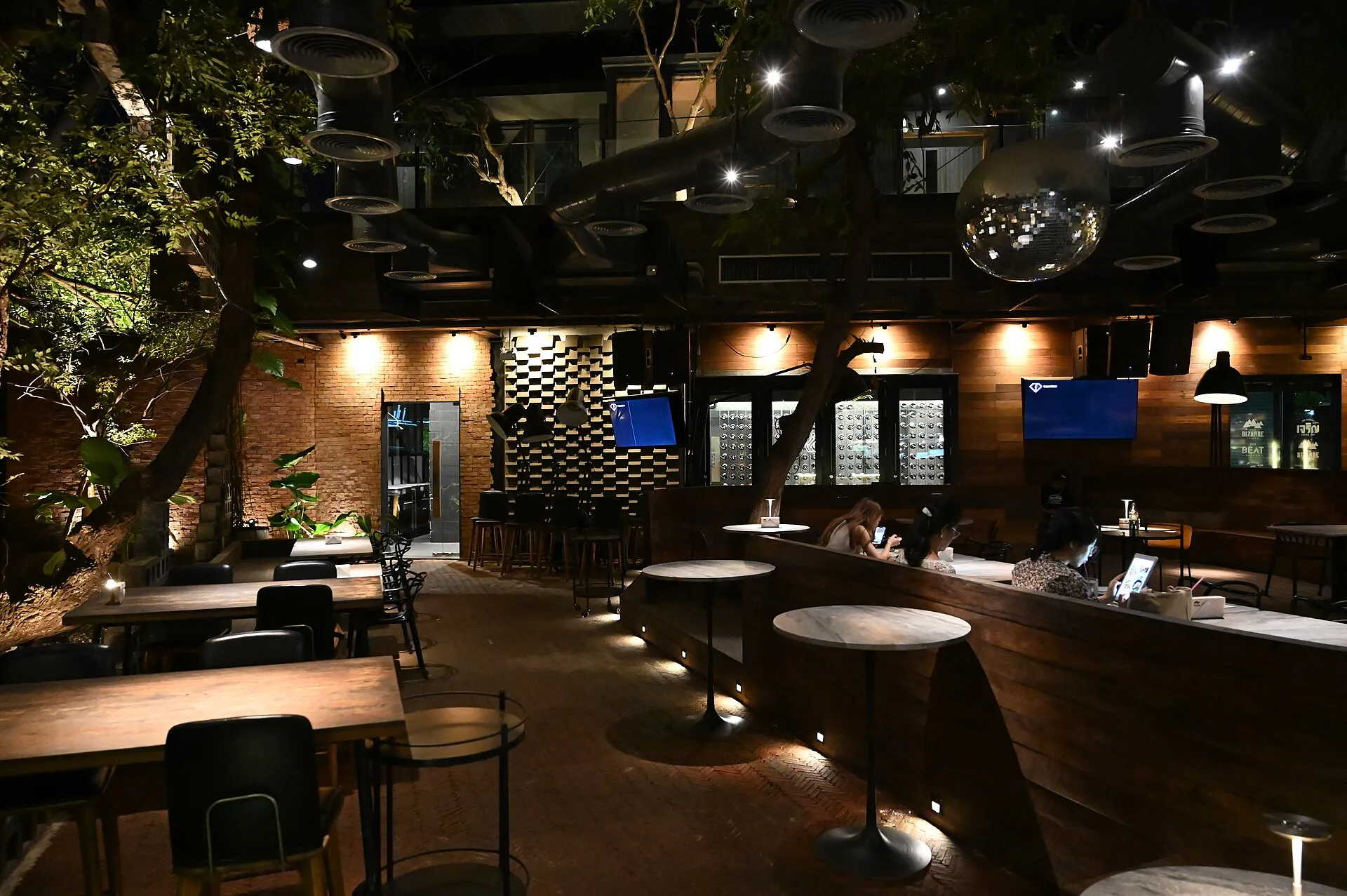 Dim café interior with warm spotlights on a brick wall, tables and planting