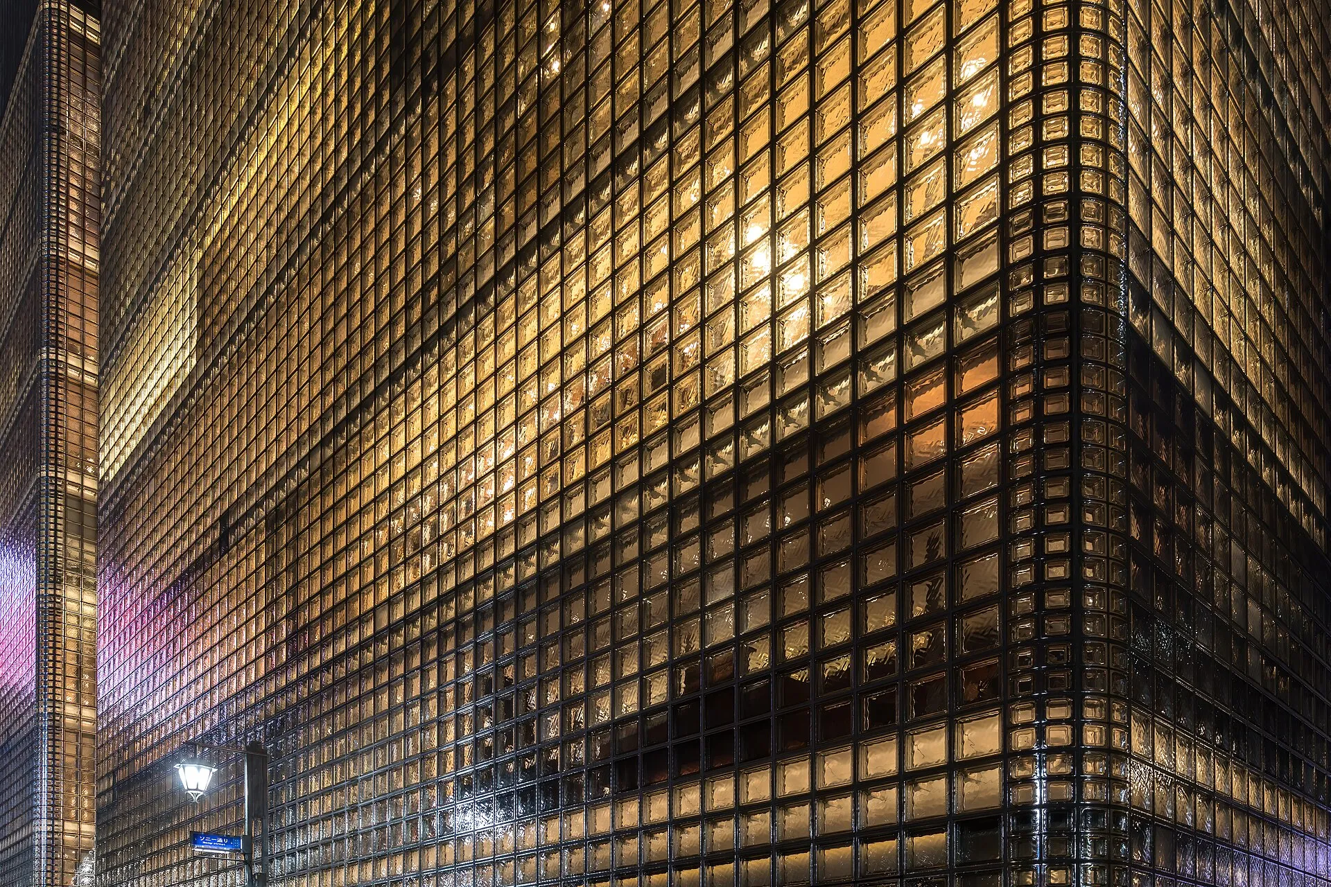 Corner of a tall glass-block facade glowing warm from inside at night